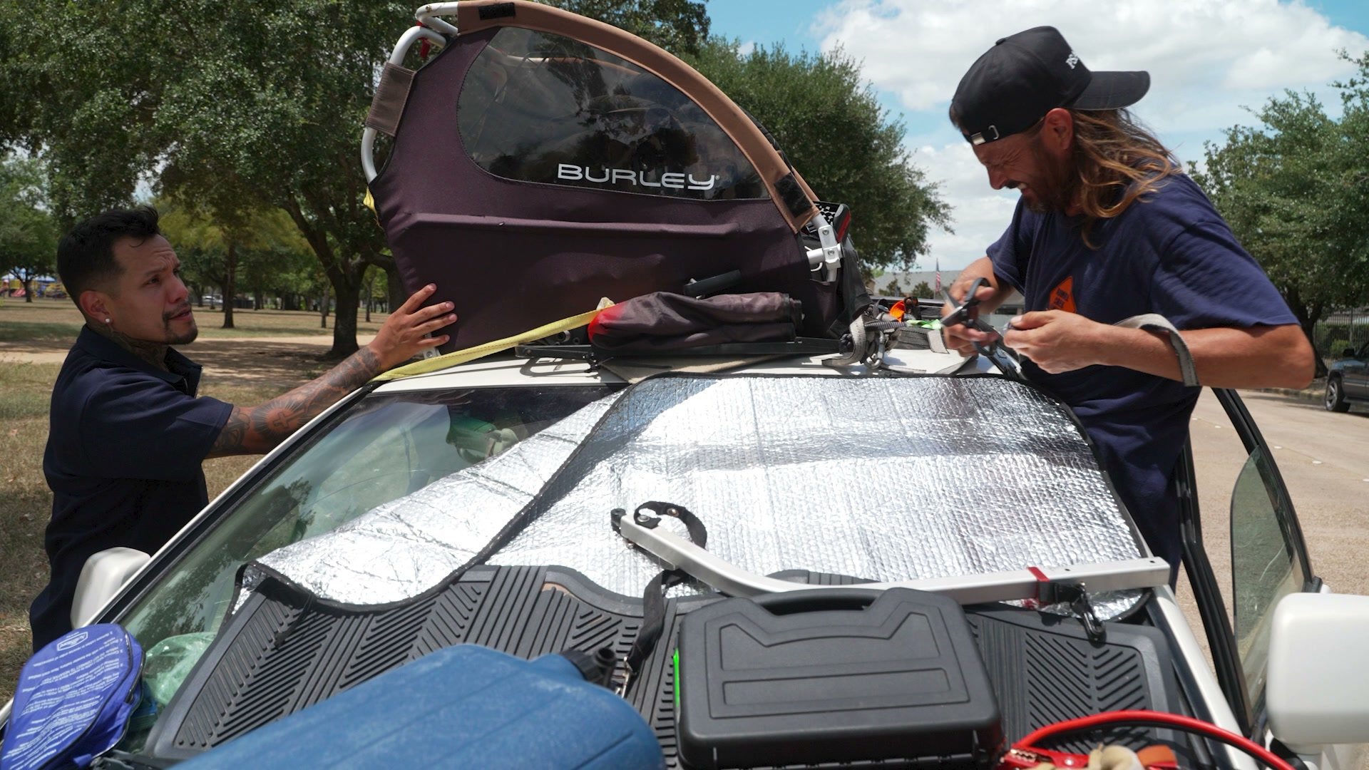 Two men strap belongings and a bike trailer to the roof of the Lexus