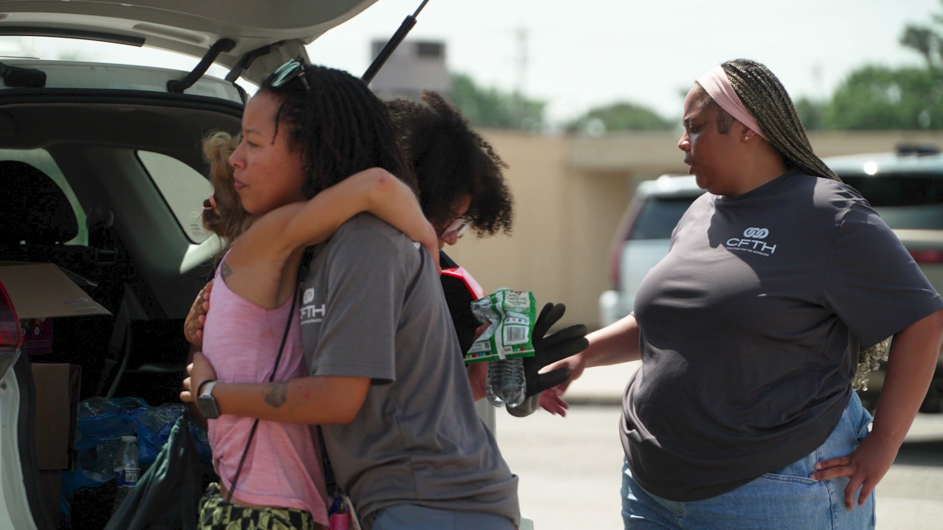 A woman in a pink shirt hugs an outreach worker beside an open car hatch