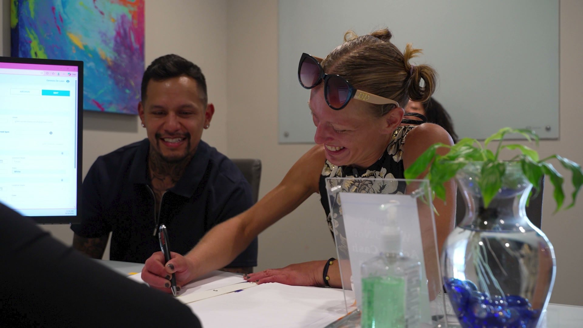 Sarah smiles as she signs paperwork at a desk beside a caseworker