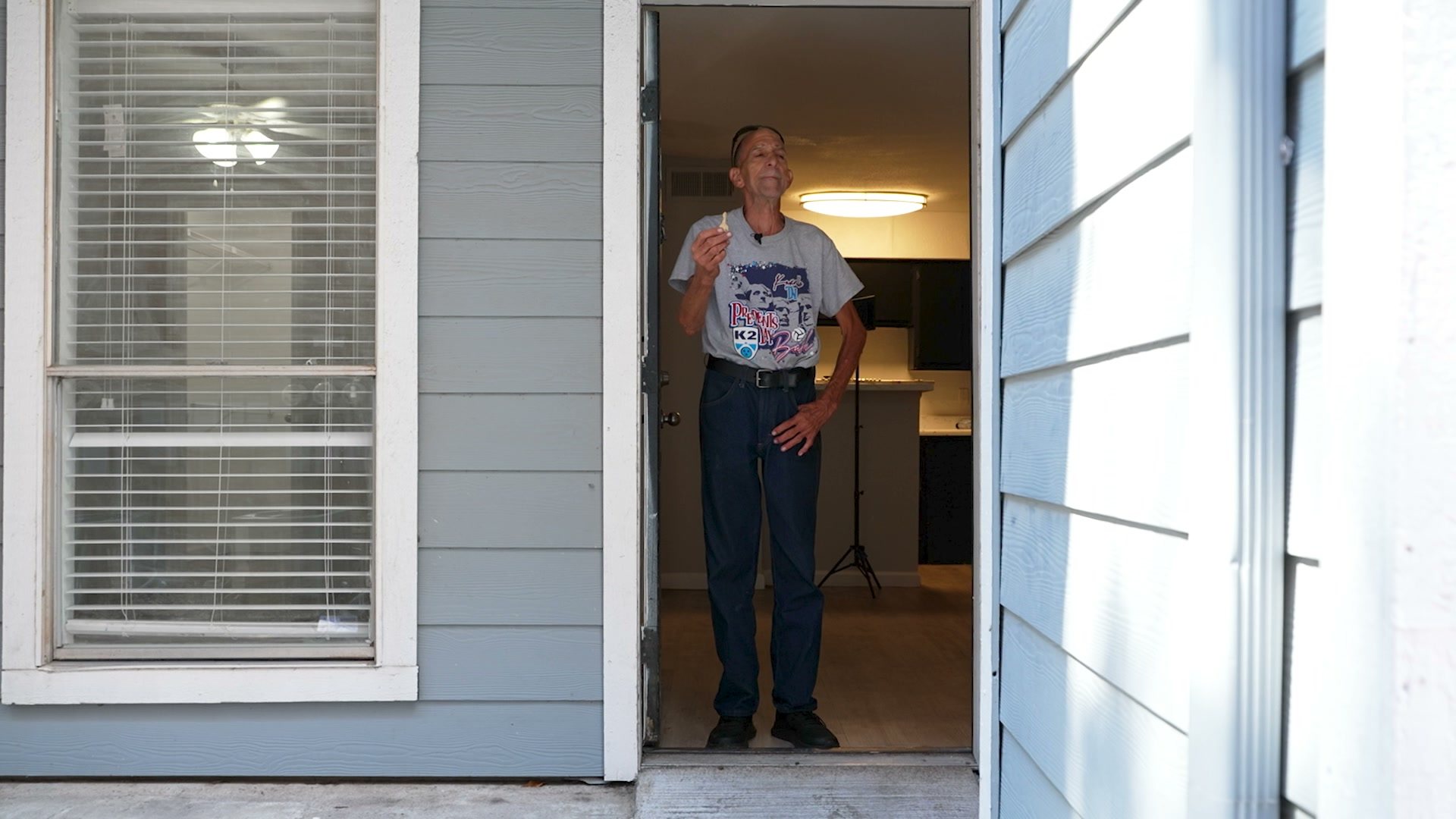 Gary stands in the open doorway of his new apartment, a light on inside