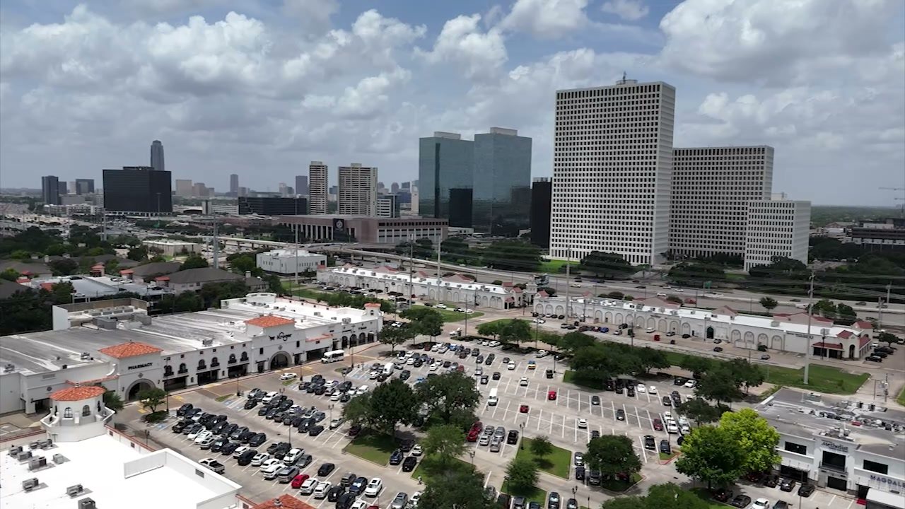 Strip-mall parking lots spread below office towers in Houston, seen from a drone